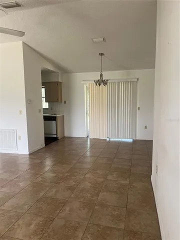 a view of an empty room and kitchen window and chandelier fan