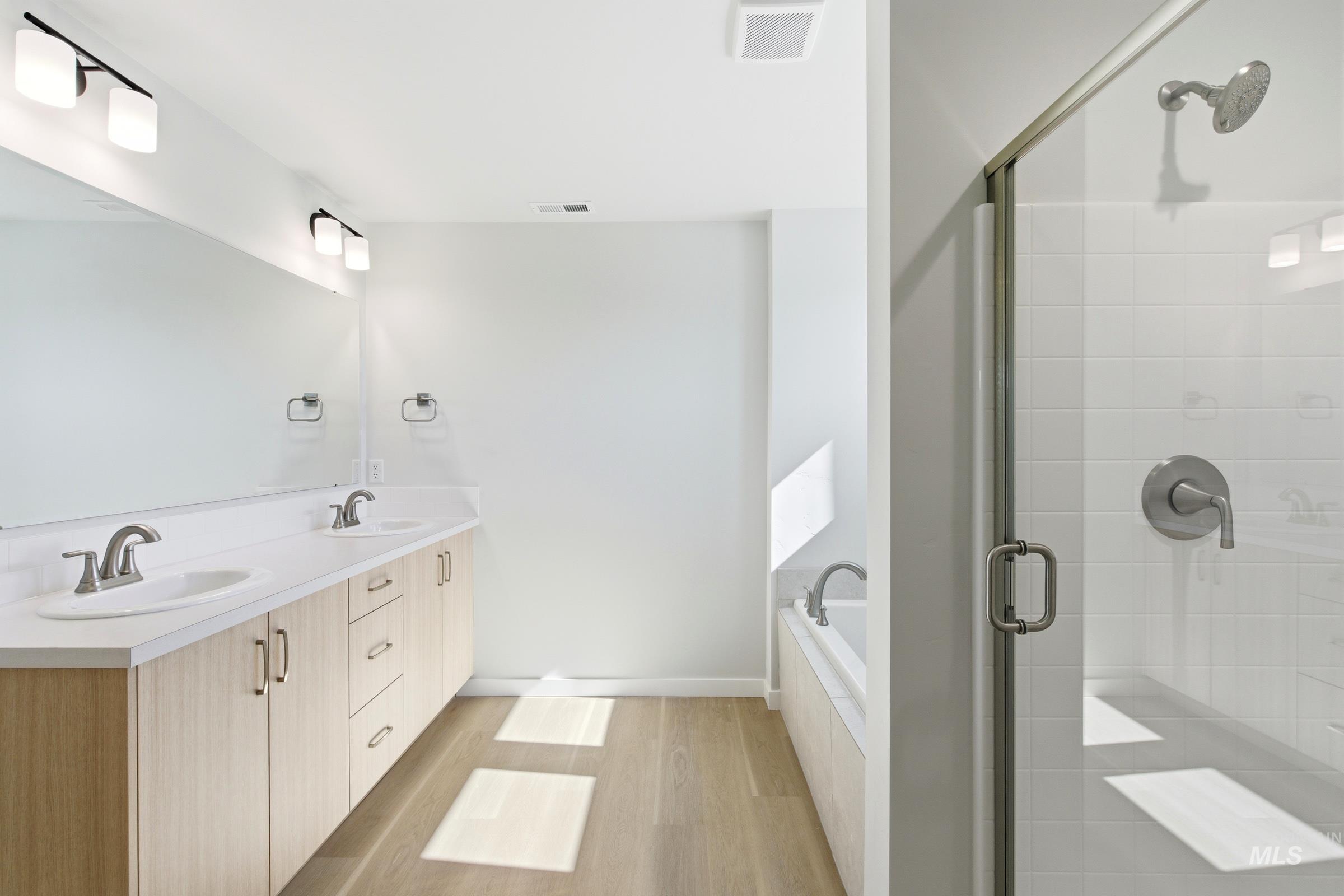13677 Redway Court Caldwell, ID 83607 - Photo 33 of 35 Spacious bathroom featuring a dual vanity with light wood-finish cabinetry and white countertops, a large frameless mirror, a walk-in shower with clear glass enclosure and subway tile surround, and a built-in soaking tub