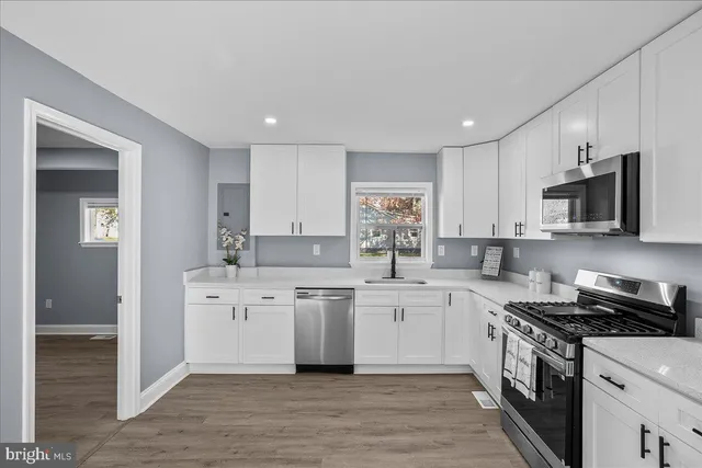 a kitchen with stainless steel appliances granite countertop a stove top oven a sink dishwasher and a refrigerator with wooden floor