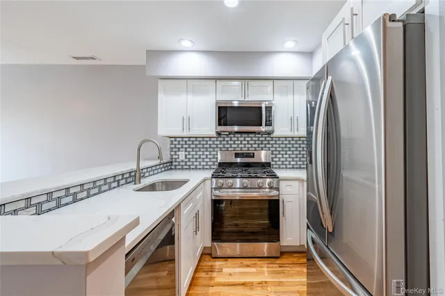 a kitchen with stainless steel appliances granite countertop a refrigerator a stove and a sink with wooden floor