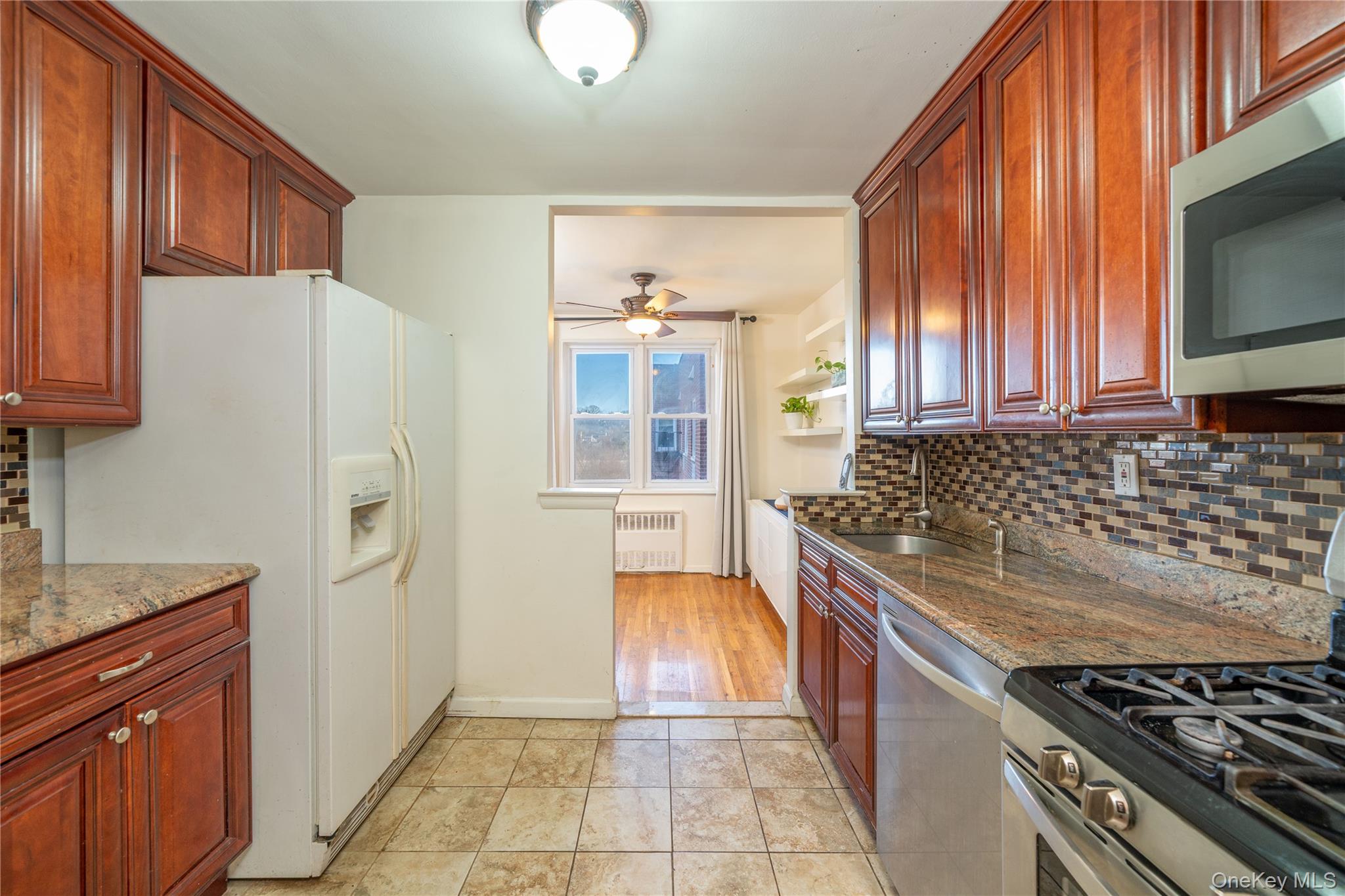495 Odell Avenue, Unit 8R Yonkers, NY 10703 - Photo 10 of 27 Kitchen featuring backsplash, stainless steel appliances, light stone counters, radiator heating unit, and dark brown cabinets