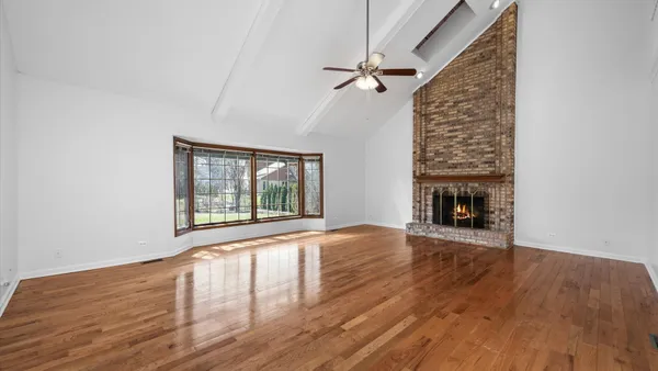 a view of an empty room with wooden floor fireplace and a window