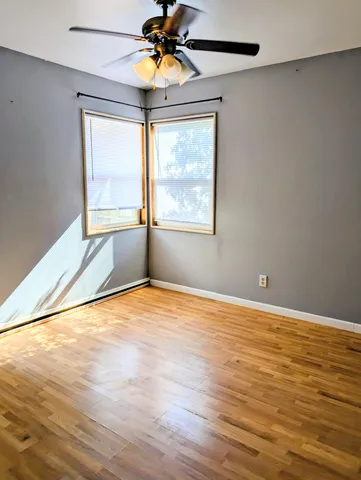an empty room with wooden floor fan and windows