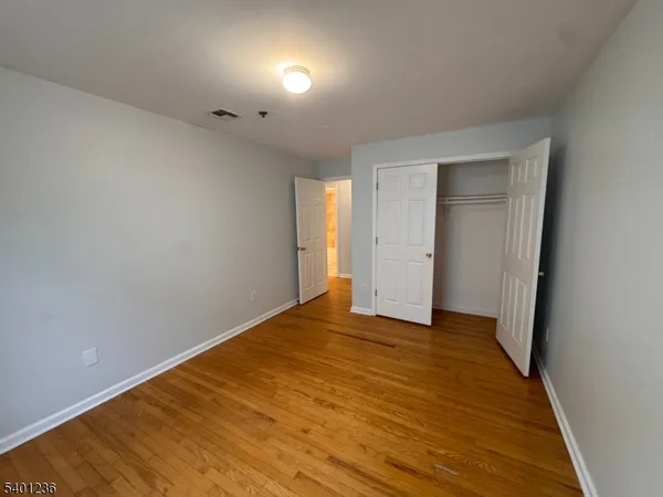 a view of an empty room with wooden floor and closet