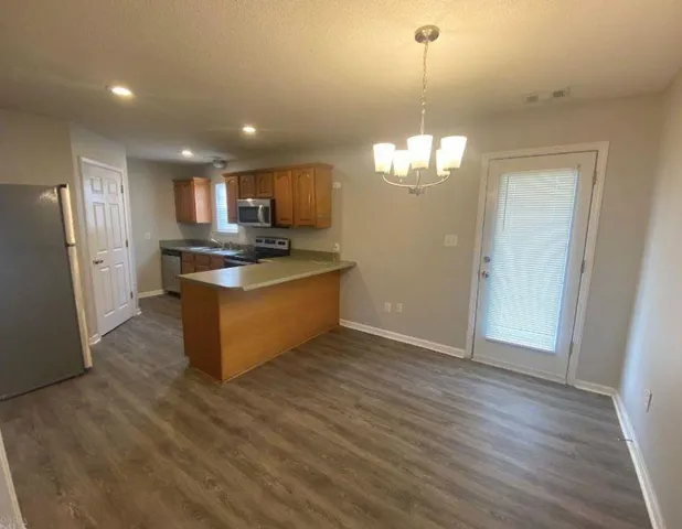 a kitchen with stainless steel appliances granite countertop a refrigerator a sink dishwasher a stove and a dining table with wooden floor