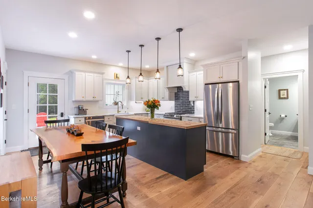 a kitchen with stainless steel appliances granite countertop a refrigerator a stove a sink a dining table and chairs with wooden floor