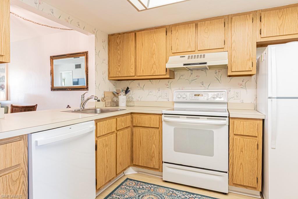 1022 Manatee Road, Unit D107 Naples, FL 34114 - Photo 17 of 43 a kitchen with stainless steel appliances granite countertop a sink a stove a refrigerator with white cabinets and wooden floor