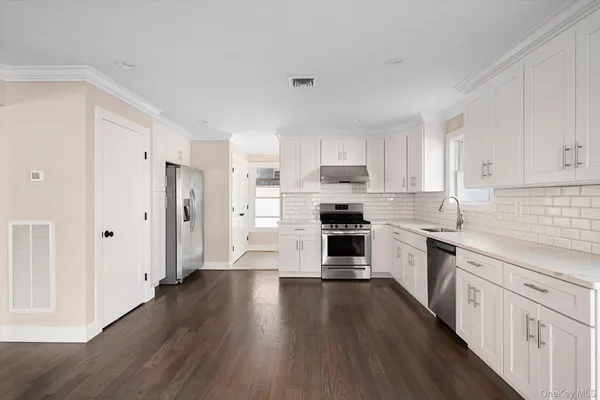 a kitchen with granite countertop a refrigerator oven a sink dishwasher and white cabinets with wooden floor