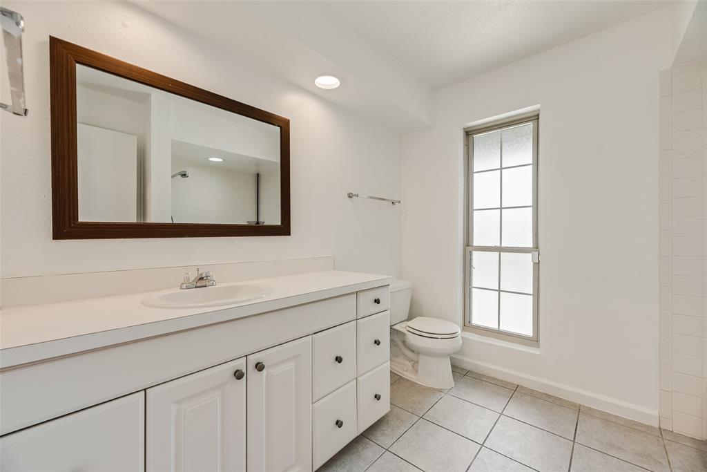 4988 Thunder Road Dallas, TX 75244 - Photo 18 of 32 Bathroom featuring a white vanity with integrated sink, a rectangular framed mirror, tile flooring, a window with frosted panes, and a commode