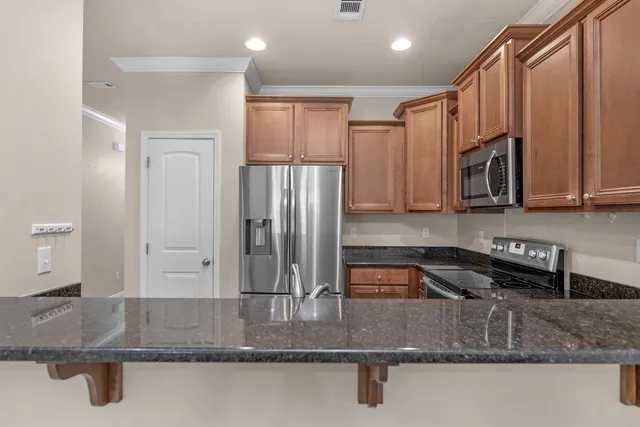 a kitchen with stainless steel appliances granite countertop a refrigerator a stove and a sink with wooden cabinets