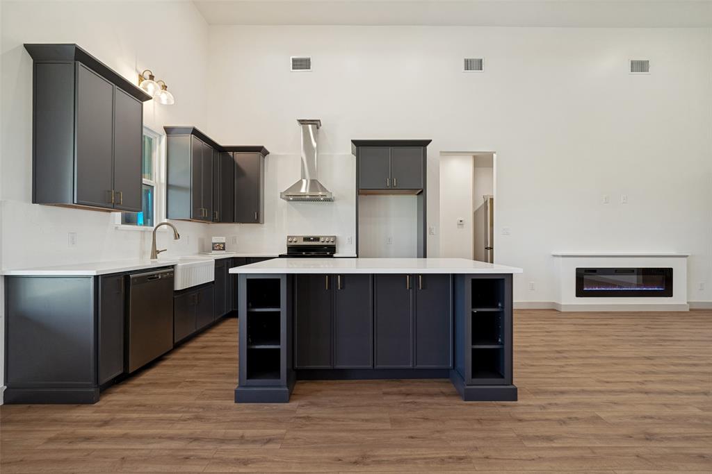 1150 Doss Road Millsap, TX 76066 - Photo 11 of 32 Spacious kitchen featuring dark cabinetry with gold-tone hardware, white countertops, a large center island with integrated shelving, and stainless steel appliances