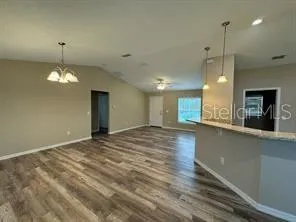a view of an empty room with wooden floor and kitchen view
