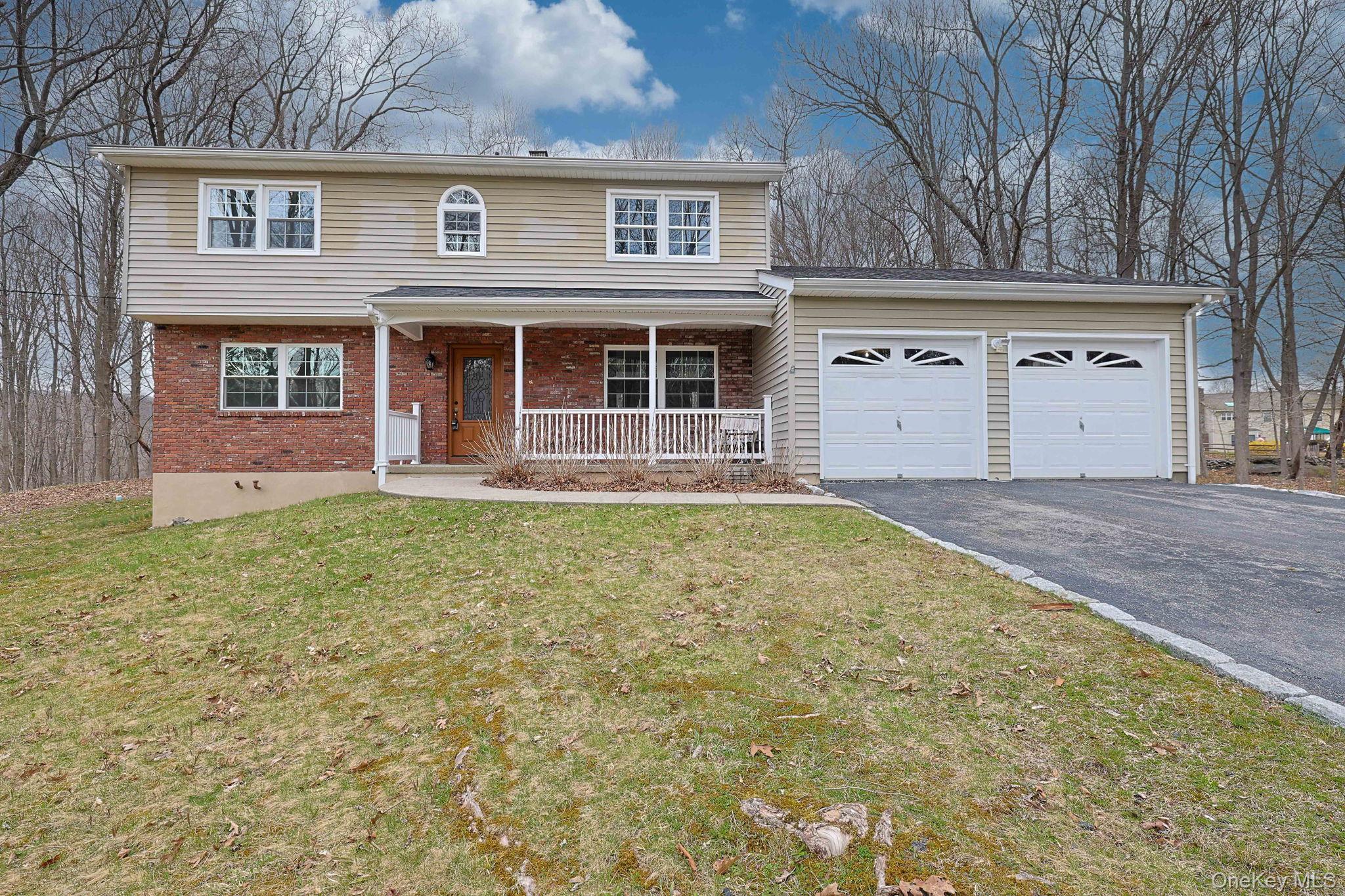 The property features a brick and siding exterior, a welcoming front porch with white railings, and a two-car garage with decorative doors