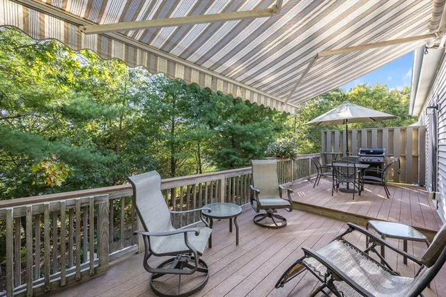 a patio table and chairs under an umbrella with wooden floor and fence