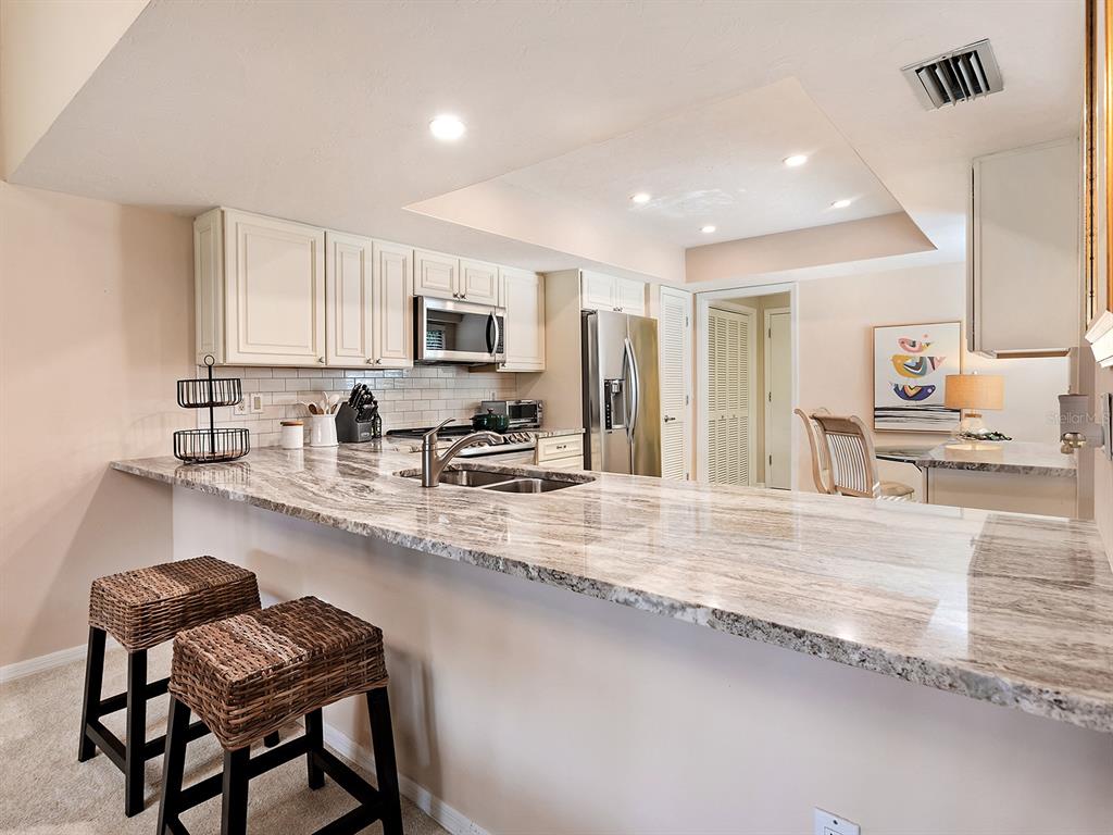 6094 Wilshire Boulevard, Unit 8 Sarasota, FL 34233 - Photo 7 of 42 a kitchen with stainless steel appliances granite countertop a stove top oven a sink a dining table and chairs