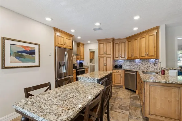 a kitchen with granite countertop kitchen island stainless steel appliances a stove refrigerator sink and wooden floor