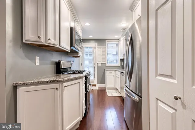 a kitchen with granite countertop a refrigerator a sink and white cabinets