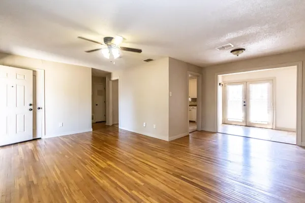 a view of an empty room with wooden floor and a ceiling fan
