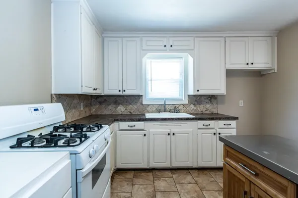 a kitchen with granite countertop a sink stove a refrigerator and cabinets