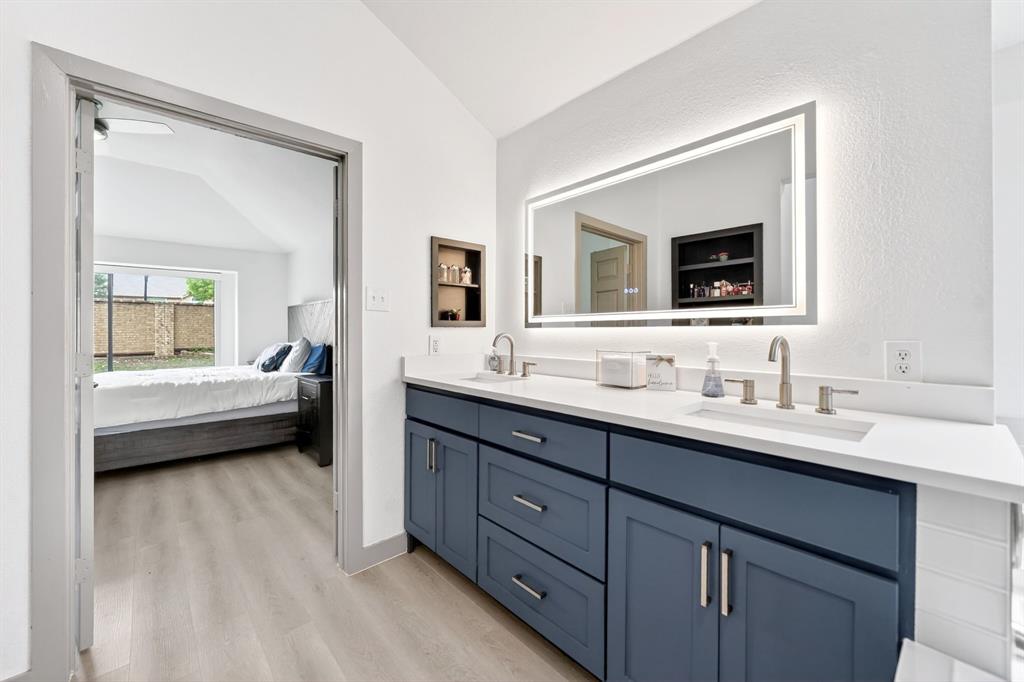 7503 Vista Ridge Lane Sachse, TX 75048 - Photo 23 of 33 The bathroom features a double vanity with a white countertop and blue cabinetry, illuminated by a large mirror with integrated lighting