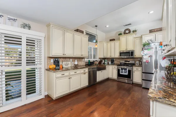 a kitchen with stainless steel appliances granite countertop a refrigerator a sink dishwasher a stove and white cabinets with wooden floor