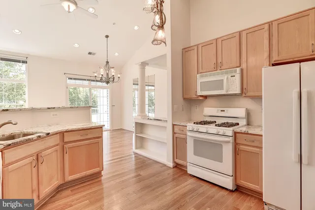 a kitchen with stainless steel appliances granite countertop a refrigerator a sink dishwasher a stove and white cabinets with wooden floor