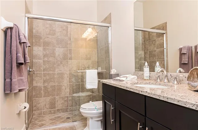 a bathroom with a granite countertop sink a toilet a mirror and shower