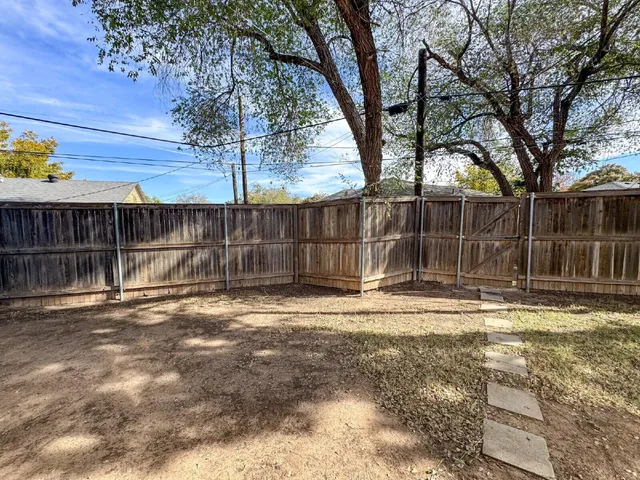 a view of a backyard with large trees and wooden fence