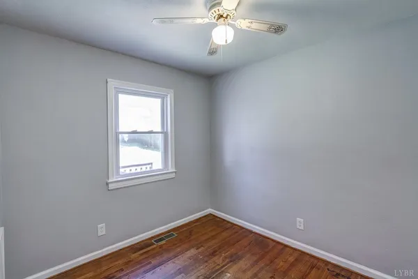 an empty room with wooden floor fan and windows
