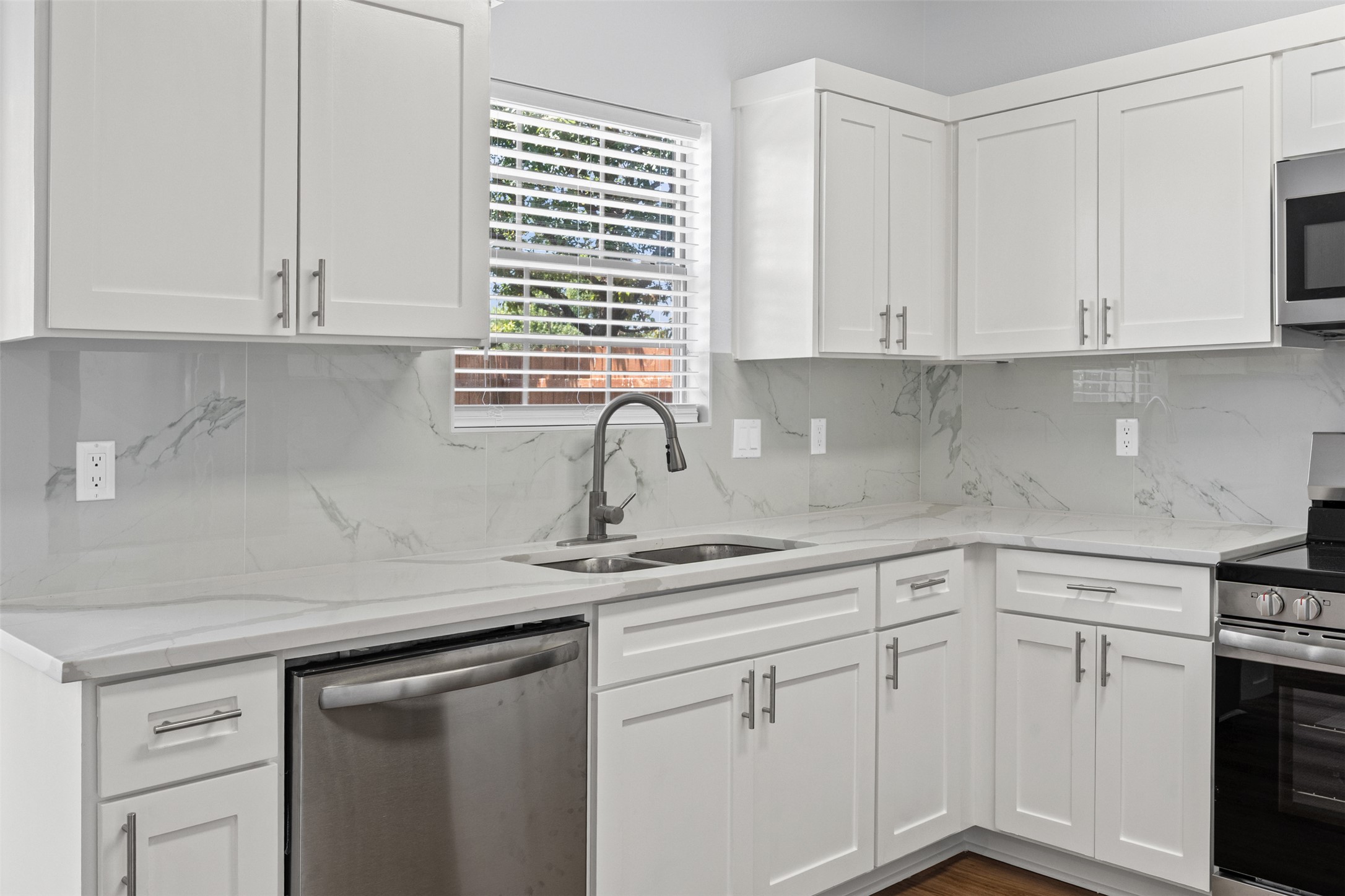243 Engineers Pass Jarrell, TX 76537 - Photo 9 of 40 Modern kitchen featuring white shaker-style cabinetry, a stainless steel double basin sink with a gooseneck faucet, and a light-toned countertop with matching backsplash