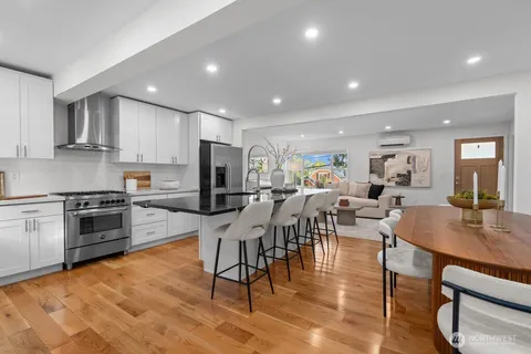 a view of kitchen with stainless steel appliances granite countertop dining table chairs stove and white cabinets