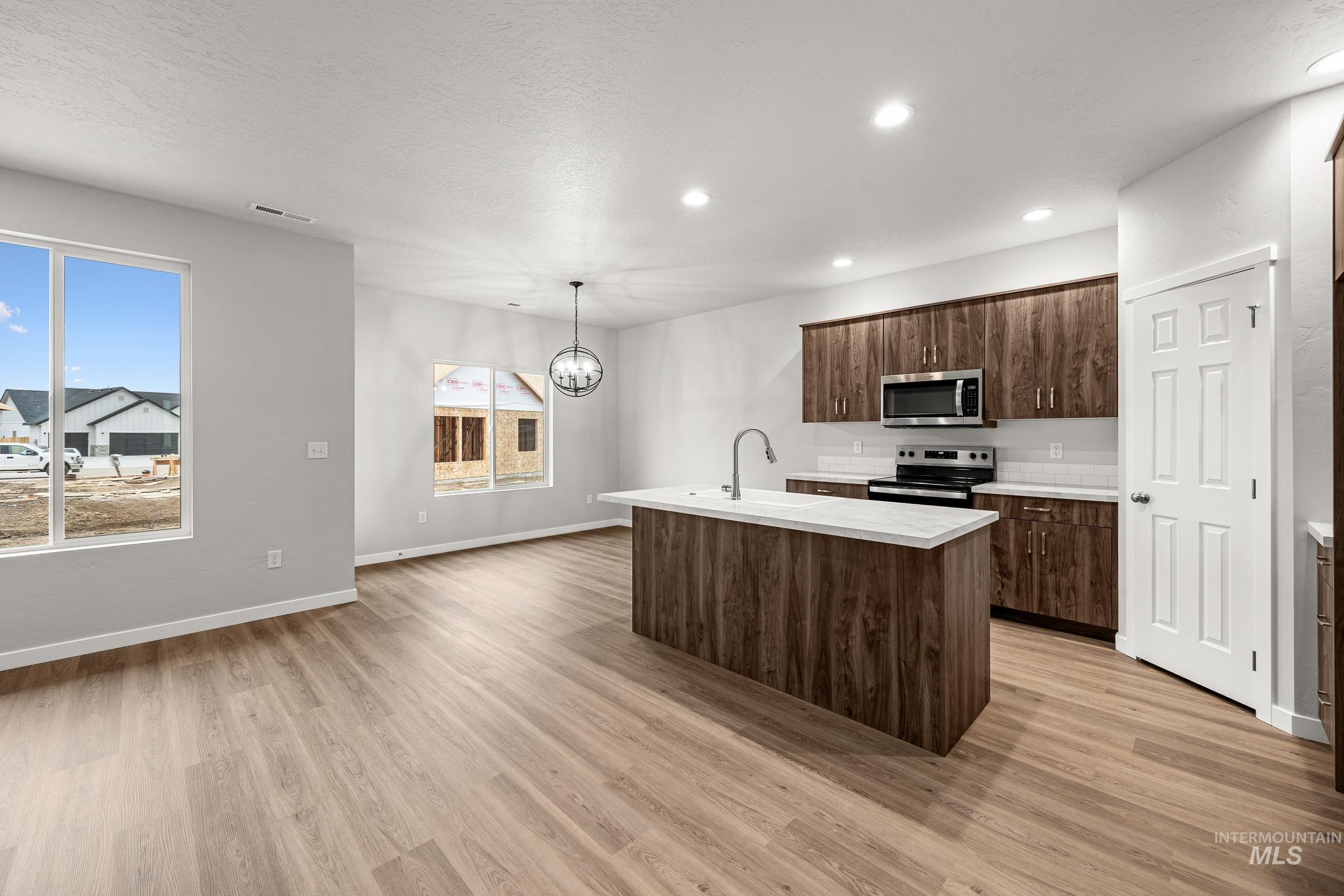13656 Redway Court Caldwell, ID 83607 - Photo 3 of 21 Kitchen featuring an island with an undermount sink and gooseneck faucet, stainless steel appliances, wood-finish cabinetry, light-toned countertops, and recessed lighting