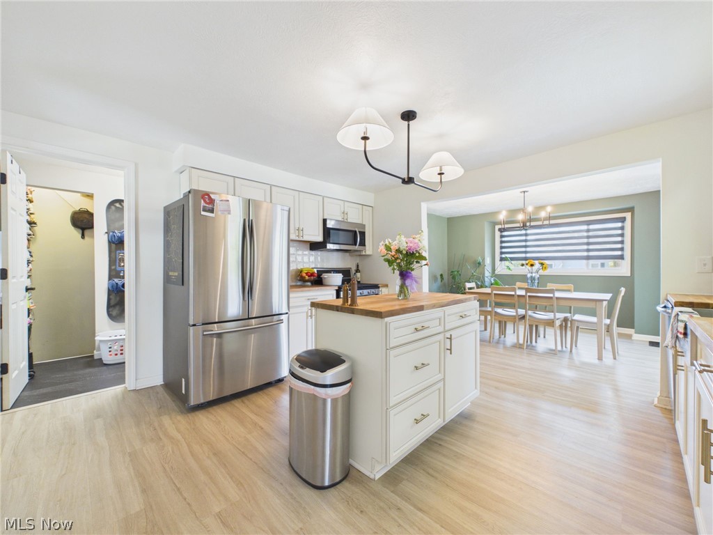 3490 County Line Road Madison, OH 44057 - Photo 23 of 42 Open-concept kitchen featuring wood-finish flooring, white cabinetry, stainless steel appliances, a center island with a butcher block countertop, and a contemporary chandelier