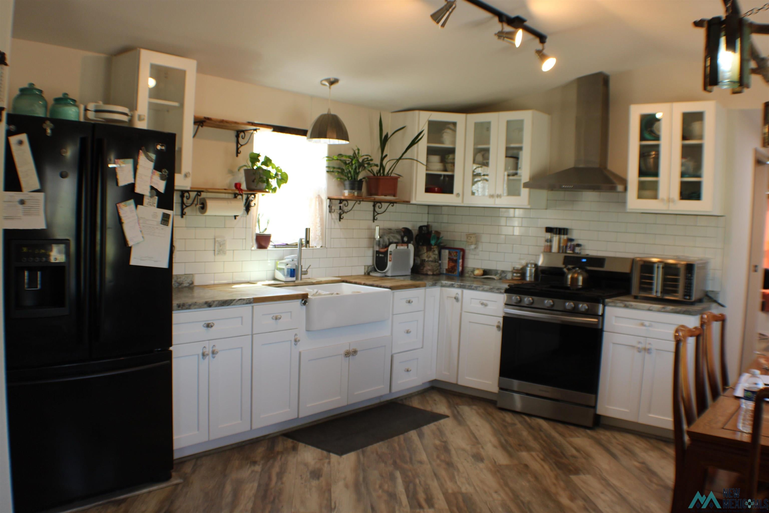 334 Animas Creek Road Caballo, NM 87931 - Photo 2 of 20 Kitchen featuring white cabinetry, a large farmhouse sink, stainless steel appliances, wood-finish flooring, and subway tile backsplash