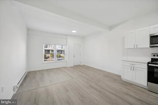 a view of an empty room with a window and a kitchen