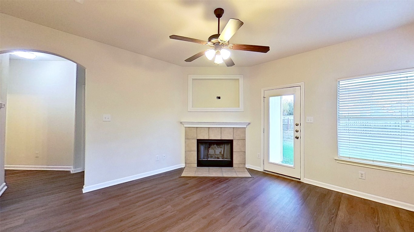 308 Rinehardt Street Hutto, TX 78634 - Photo 14 of 30 Unfurnished living room featuring ceiling fan, a tile fireplace, dark wood-type flooring, and arched walkways