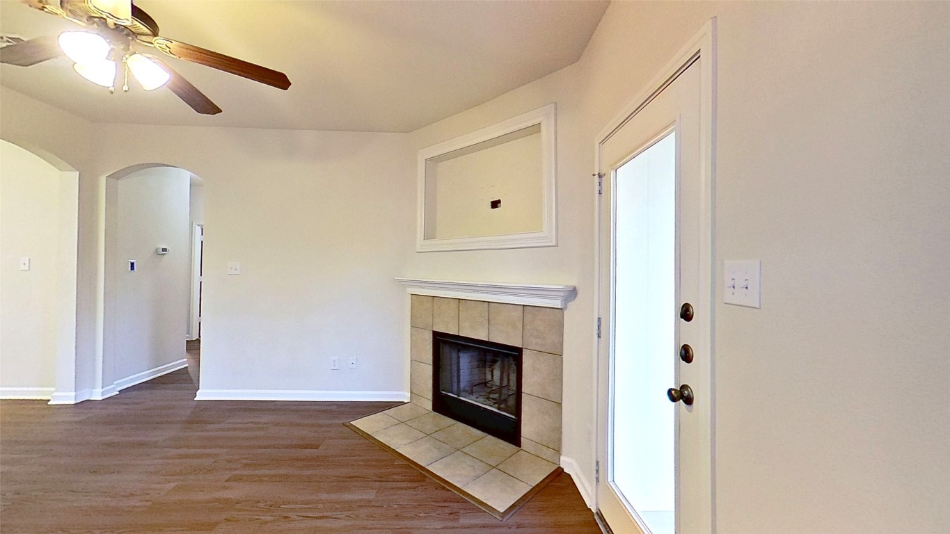 308 Rinehardt Street Hutto, TX 78634 - Photo 3 of 30 Unfurnished living room with arched walkways, dark wood-style flooring, a fireplace, and a ceiling fan