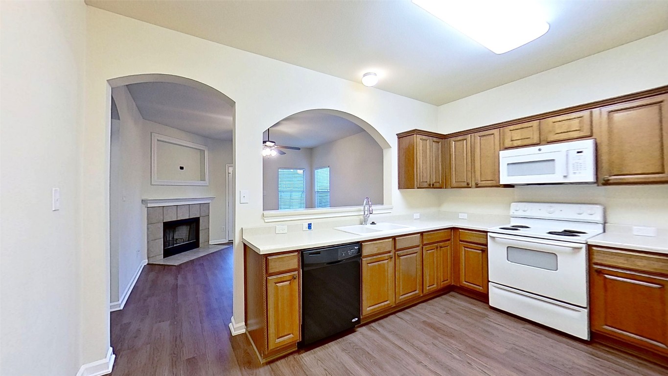308 Rinehardt Street Hutto, TX 78634 - Photo 10 of 30 Kitchen featuring white appliances, a tile fireplace, light countertops, dark wood-style flooring, and a ceiling fan