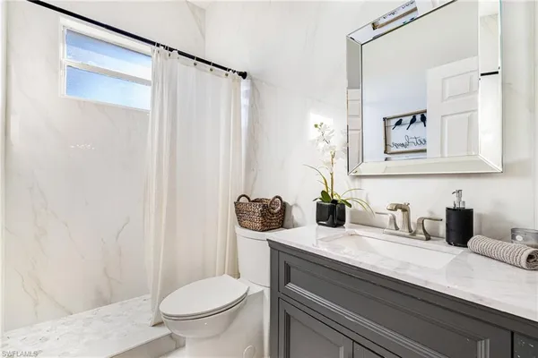 a bathroom with a granite countertop sink a toilet a mirror and shower curtain