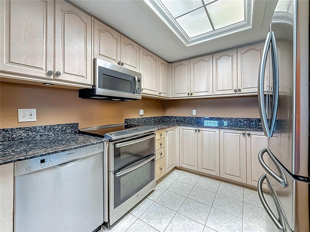 399 150th Avenue, Unit 317 Madeira Beach, FL 33708 - Photo 18 of 96 a kitchen with stainless steel appliances granite countertop a refrigerator oven a sink dishwasher and white cabinets next to a window