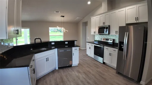 a kitchen with stainless steel appliances granite countertop a sink a stove a refrigerator a window and wooden floor