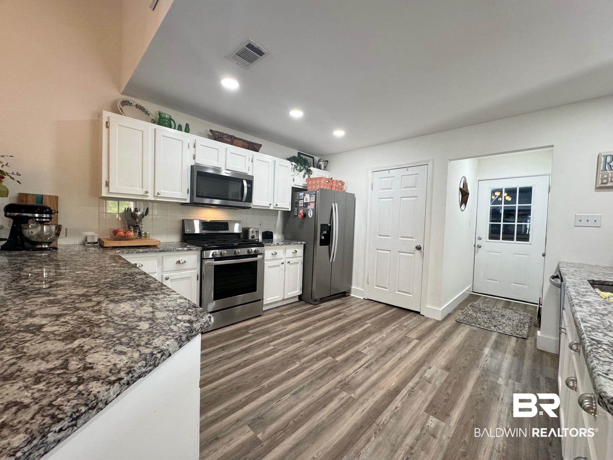 3200 Loop Road, Unit 55 Orange Beach, AL 36561 - Photo 12 of 40 Kitchen with tasteful backsplash, dark wood-type flooring, dark stone counters, white cabinetry, and appliances with stainless steel finishes
