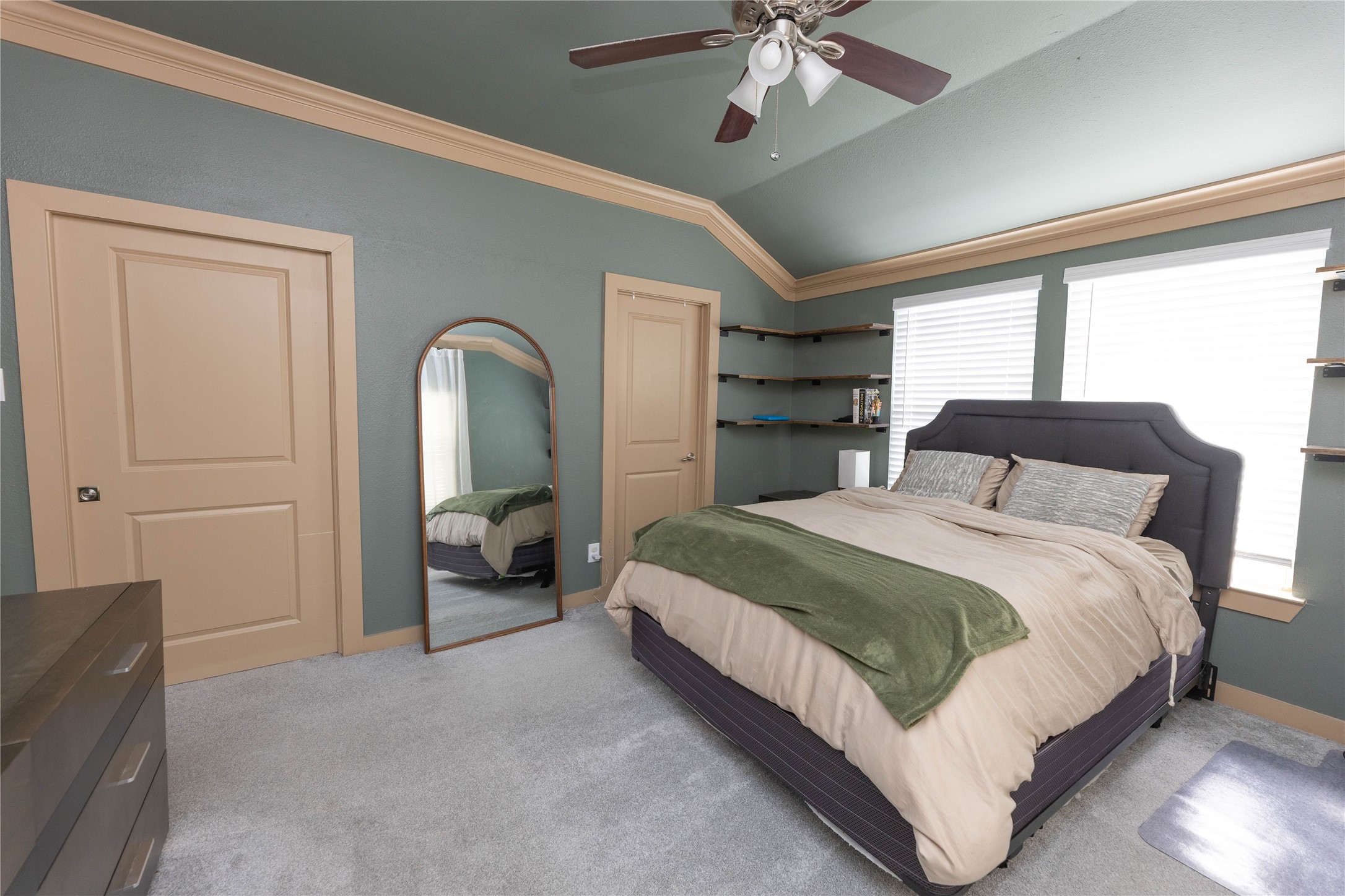 8007 Capitol Street Houston, TX 77012 - Photo 16 of 25 This bedroom features a modern ceiling fan, soft carpeting, and ample natural light from two windows. The walls are accented with wood trim, and a large mirror and open shelves add functionality and style.