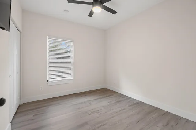 an empty room with wooden floor fan and windows