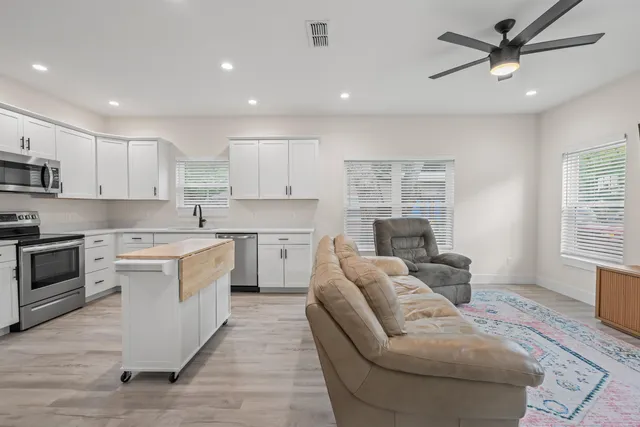 a large white kitchen with a stove a sink a kitchen island with a dining table and chair