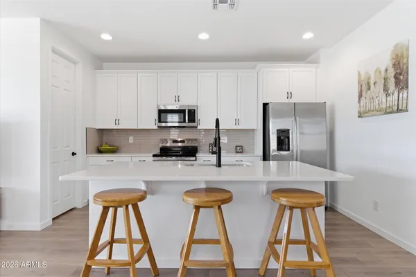 a kitchen with stainless steel appliances granite countertop a stove top oven a sink a refrigerator with white cabinets and wooden floor
