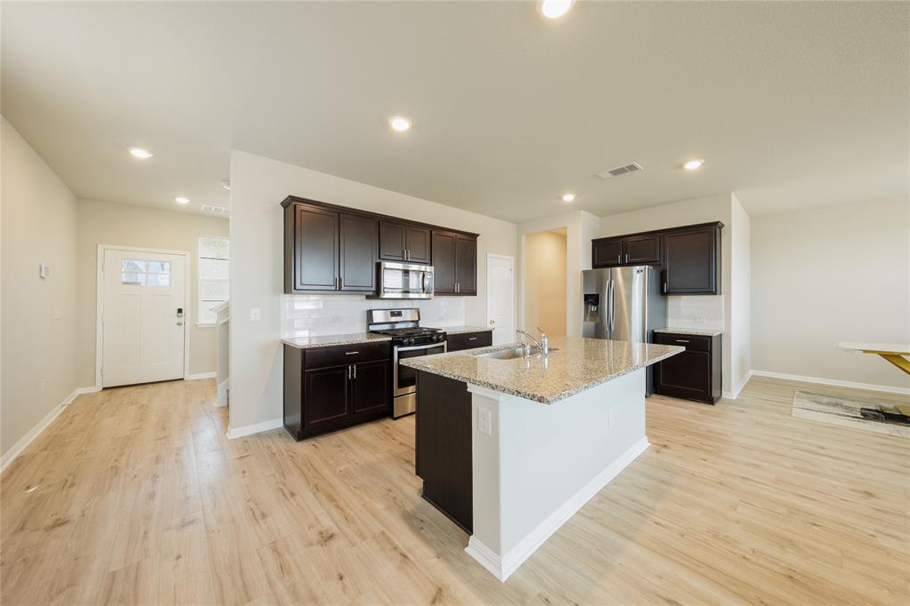 521 Otto Avenue Georgetown, TX 78626 - Photo 7 of 38 Kitchen with stainless steel appliances, dark wood finish cabinetry, a kitchen island with sink, light stone counters, and recessed lighting
