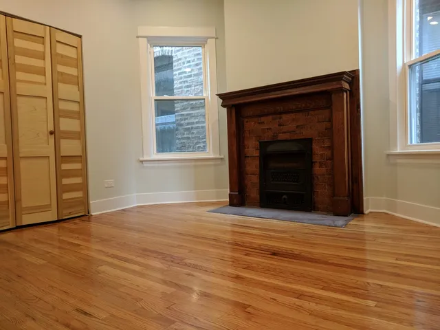 an empty room with wooden floor fireplace and windows