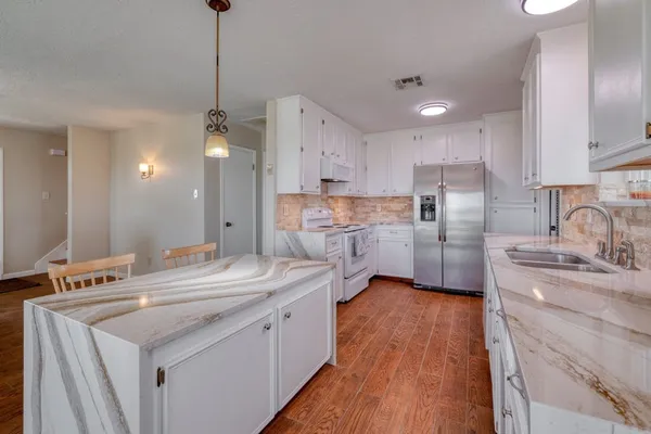 a kitchen with stainless steel appliances a sink dishwasher a stove a refrigerator and island with wooden floor
