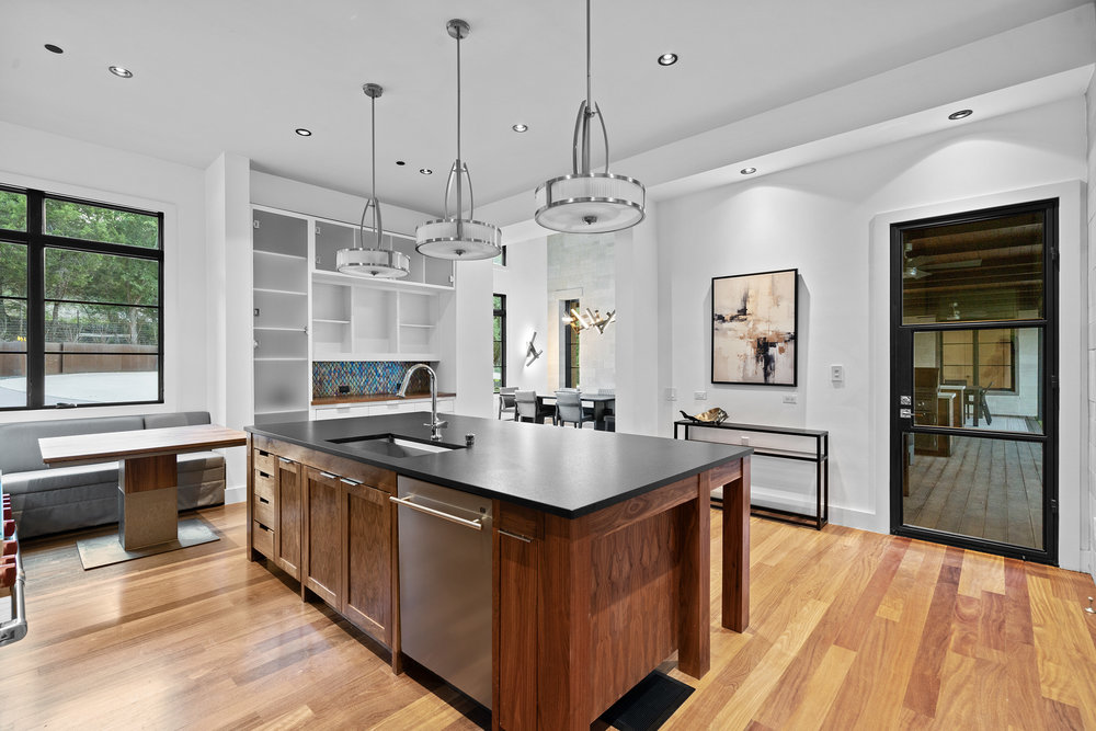 1905 Paisano Road Austin, TX 78746 - Photo 8 of 40 Custom cabinetry and built-in features define this modern kitchen with warm wood flooring and integrated appliances.